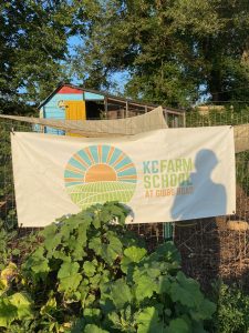 a farm landscape with a flowering bush and a sign that reads "KC Farm School at Gibbs Road"